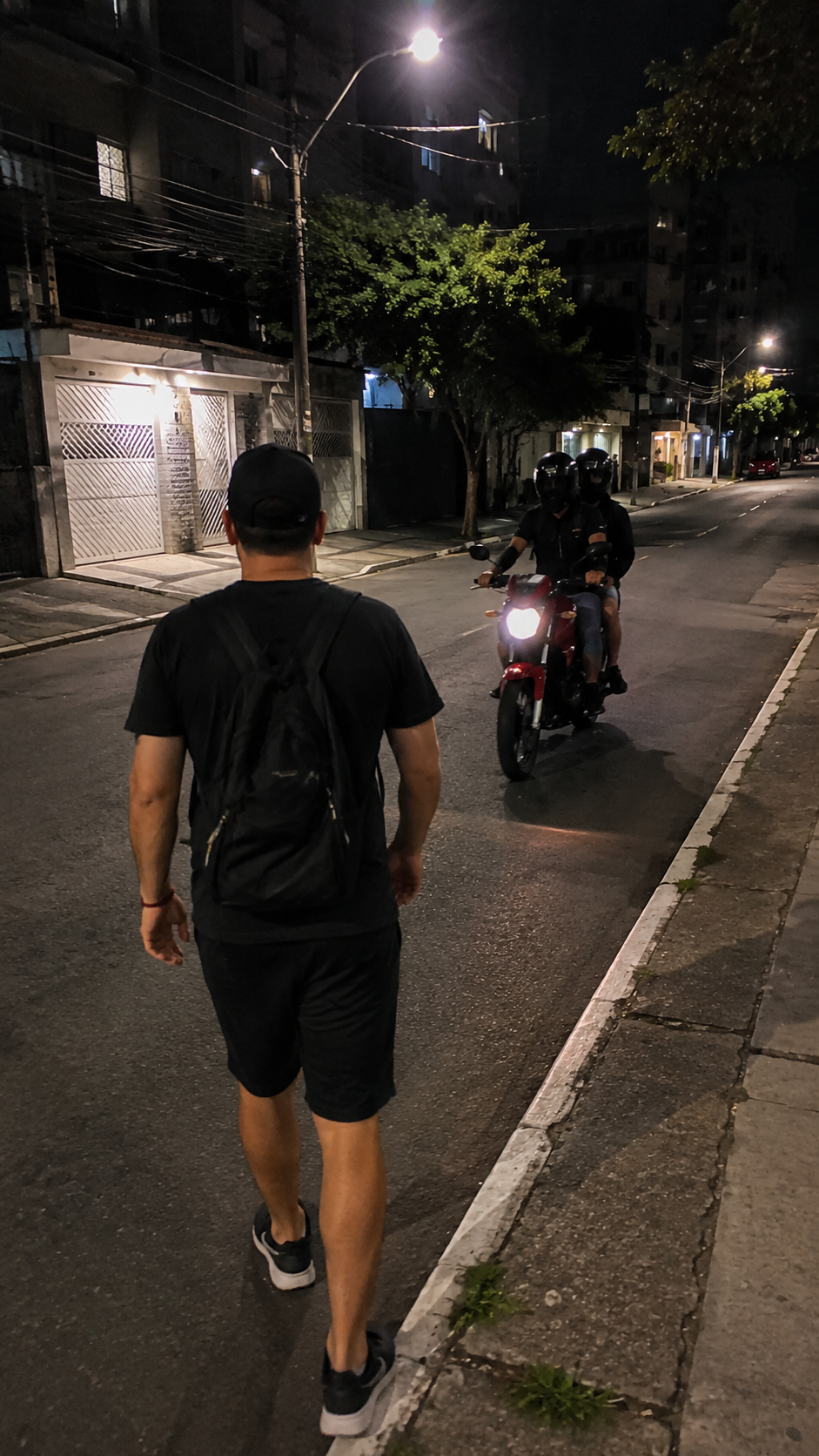 Pessoa caminhando à noite enquanto uma moto se aproxima